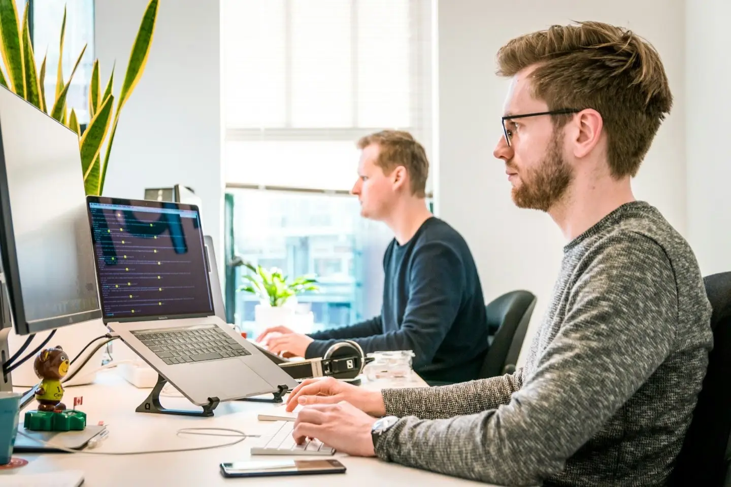 Zwei Mitarbeiter an Arbeitsplätzen mit Notebooks und Monitoren